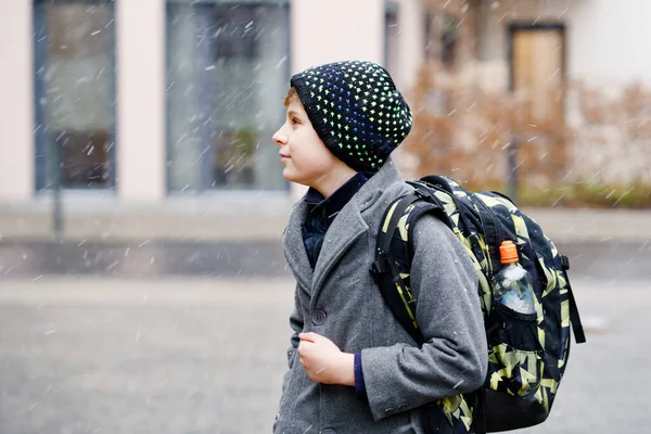 Retrato de un niño preadolescente al aire libre. Niño guapo en abrigo y sombrero en invierno. Escolar en el camino a la escuela con mochila durante la nieve — Foto de Stock