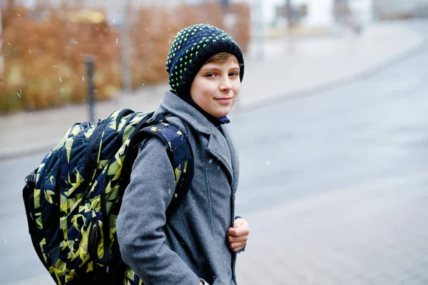 Açık havada ergen bir çocuğun portresi. Kışın paltolu ve şapkalı yakışıklı çocuk. Okul çocuğu kar yağarken sırt çantasıyla okula gidiyor. — Stok fotoğraf