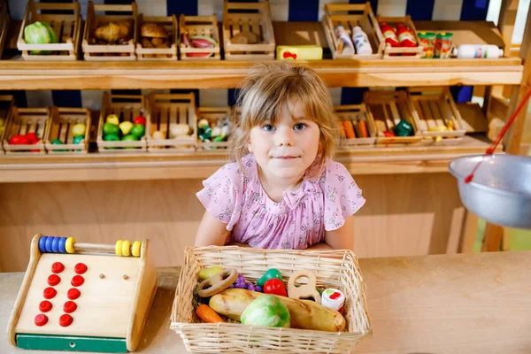 La bambina in età prescolare gioca con il cibo e giocattoli di legno della drogheria. Felice gioco di ruolo bambino attivo come cassiere o venditore, in negozio di legno o supermercato. Educazione, attività per bambini. — Foto Stock