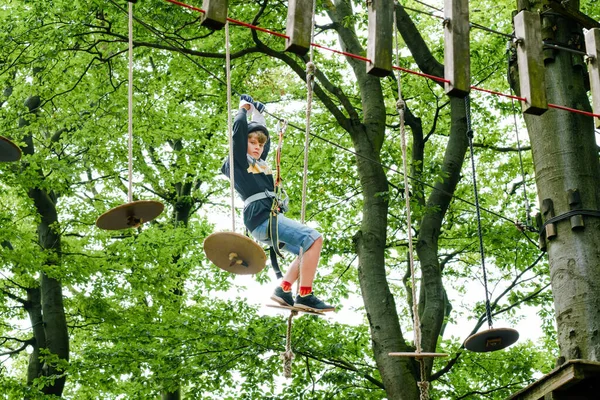 Orman macera parkındaki okul çocuğu. Aktif çocuk, kask takan çocuk yüksek ip izine tırmanıyor. Çeviklik becerileri ve çocuklar için açık hava eğlence merkezine tırmanma. Çocuklar ve aileler için açık hava aktivitesi. — Stok fotoğraf