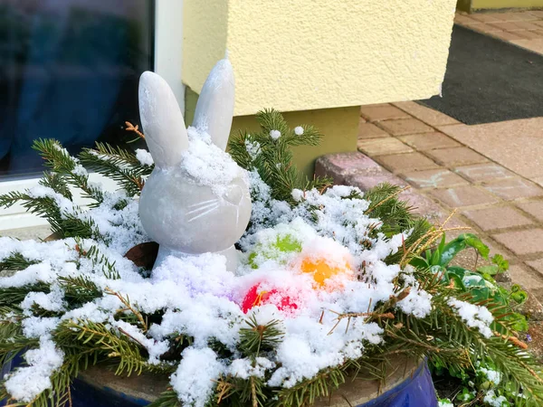 Paskalya açık hava dekorasyonu karla kaplı. Paskalya tavşanı ve renkli yumurtalar dışarıda büyük bir kasede. Soğuk ve geç bahar, Nisan 'da kar yağışı. — Stok fotoğraf