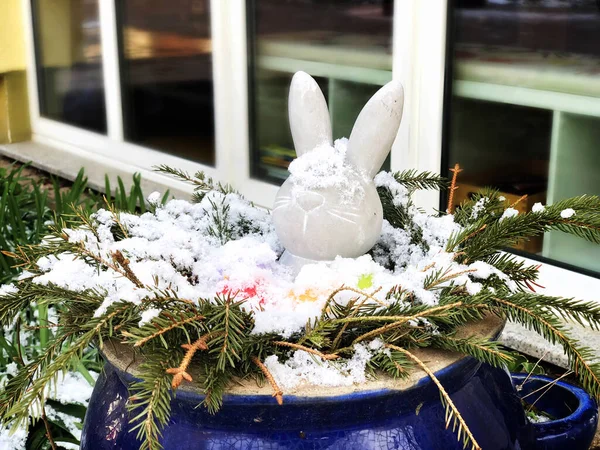 Easter outdoors decoration covered with snow. Easter bunny and colored eggs in a big bowl outside. Cold and late spring, snowfall in April. — Stock Photo, Image
