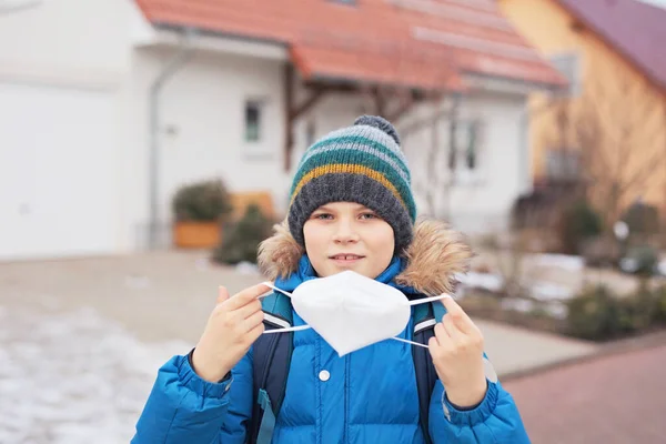 Grabben bär mask på väg till skolan. En ryggsäck för barn. Skolbarn på kall höst eller vinter dag med varma kläder. Nedstängning och karantänstid under koronapandemisk sjukdom — Stockfoto