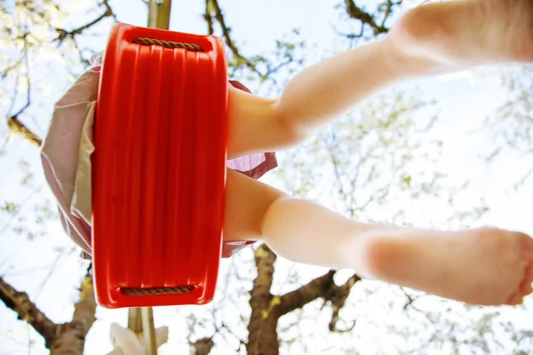 Close-up van de voeten van kleine peuter meisje plezier hebben op schommel in de binnenlandse tuin. Klein kind swingend onder bloeiende bomen op zonnige dag. Actieve vrijetijdsbesteding en buitenactiviteiten — Stockfoto