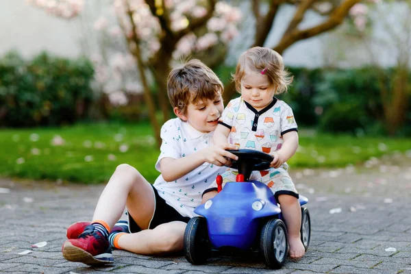 Cute little baby girl and school kid boy playing with blue small toy car in garden of home or nursery. Toddler sister and brother children having fun together. — Stock Photo, Image