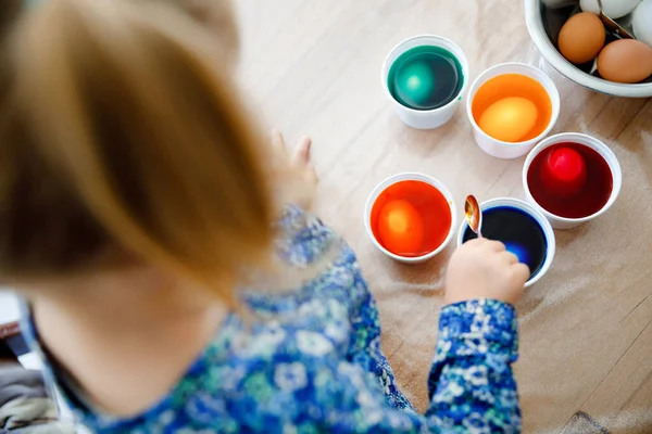 Closeup of little toddler girl coloring eggs for Easter. Close-up of child looking surprised at colorful colored eggs, celebrating holiday with family. From above, unrecognized face. — Stock Photo, Image