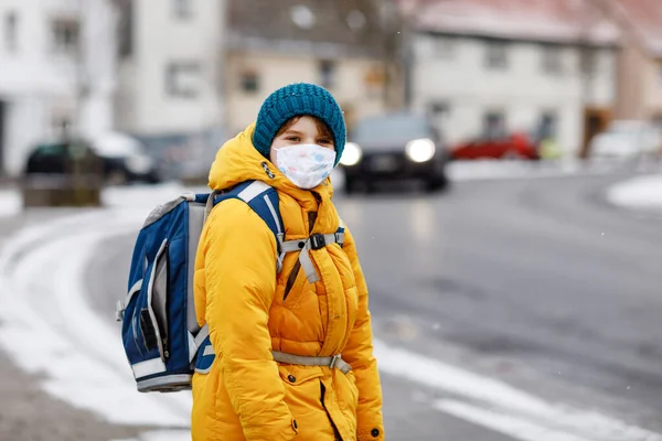 Little kid boy wearing medical mask on the way to school. Child backpack satchel. Schoolkid on cold autumn or winter day with warm clothes. Lockdown and quarantine time during corona pandemic disease — Stock Photo, Image