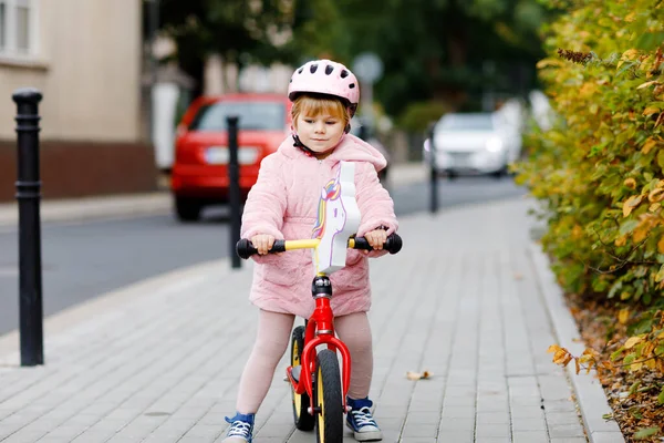 Söt liten småbarnstjej med hjälm på springcykel till dagis, lekskola eller förskola. Glad barn har kul med att lära sig på elev cykel. Aktiv unge på kall höstdag utomhus. — Stockfoto