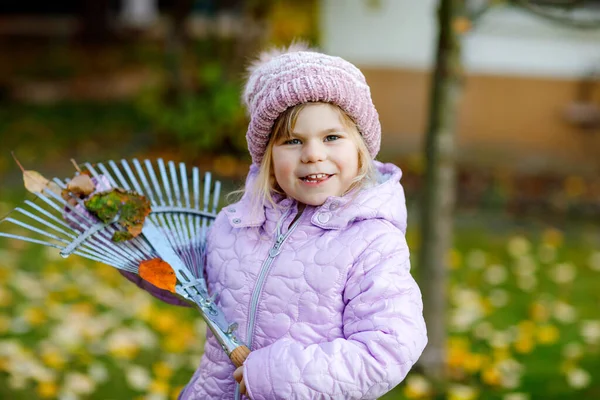 Pequena menina criança trabalhando com ancinho no jardim de outono ou parque. Criança saudável feliz adorável que se diverte com a ajuda de folhas caídas de árvores. Ajudante bonito ao ar livre. aprendizagem da criança ajuda pais — Fotografia de Stock