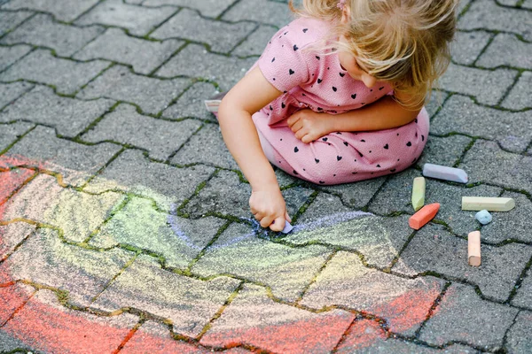 Pequena menina pré-escolar pintando arco-íris com giz colorido no chão no quintal. Criança feliz positiva desenhando e criando imagens. Atividades criativas ao ar livre no verão. — Fotografia de Stock