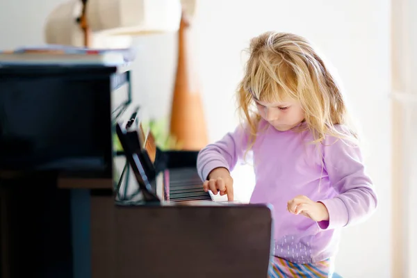 リビングルームでピアノを弾いている美しい小さな幼児の女の子。楽器を演奏することを学ぶことで楽しいかわいい就学前の子供。子供のための初期の音楽教育. — ストック写真