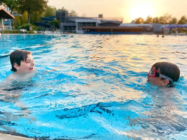 Dos niños de la escuela jugando y chapoteando en una piscina al aire libre en el cálido día de verano. Niños felices y sanos disfrutando de un clima soleado en la piscina pública de la ciudad. Actividad infantil al aire libre con agua. — Foto de Stock