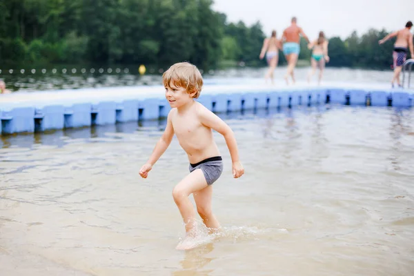 Little blond preschool boy having fun with splashing in a lake on summer day, outdoors. Happy child learning swimming. Active leisure with kids on vacations. Danger on domestic lakes — Stock Photo, Image