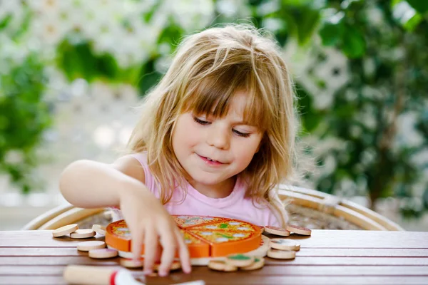 Malá roztomilá dívka hraje s dřevěnou hračkou pizzu. Mládež ve školce baví s dětmi aktivity jako, hrát si s jídlem, uvnitř. — Stock fotografie