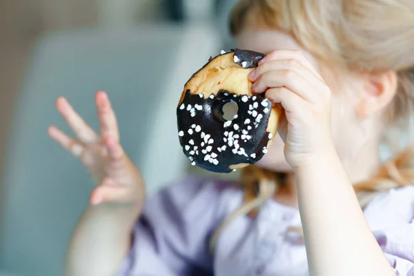 Boldog kis óvodás lány, aki édes fánkot eszik. Szőke gyerek a városban. Aranyos gyerek és egészségtelen cukros fánk.. — Stock Fotó