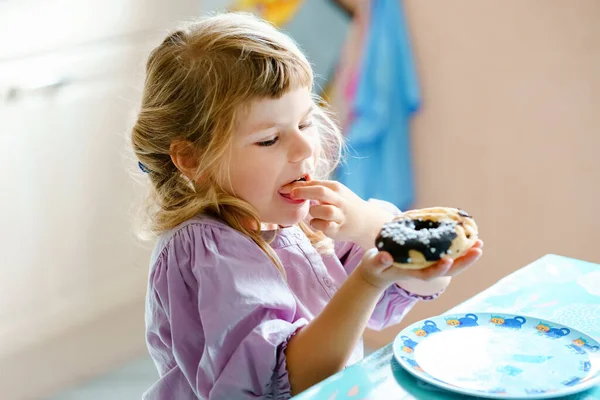 幸せな小さな就学前の女の子甘いドーナツ屋内を食べる。市内の金髪の子供。かわいい子供と不健康な砂糖入り食品ドーナツ. — ストック写真