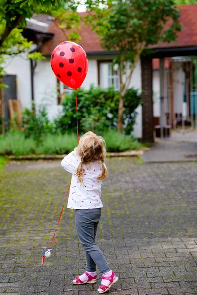Roztomilý šťastný školačka hrát s beruška balón venku. Malé dítě slaví narozeniny. — Stock fotografie