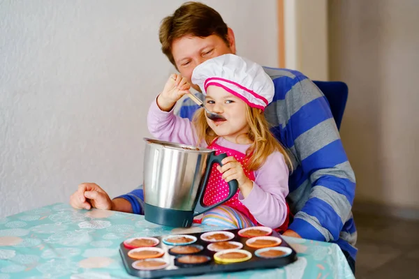 Linda niña pequeña y padre hornear magdalenas de chocolate caseras magdalenas en el hogar en interiores. Feliz niño preescolar y papá juntos en la cocina doméstica. —  Fotos de Stock