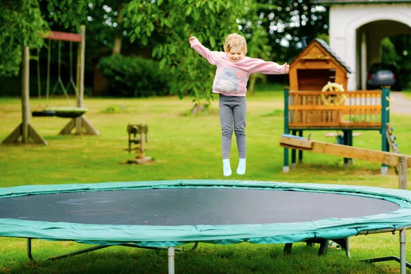 Uma miúda pré-escolar a saltar em trampolim. Criança engraçada feliz se divertindo com a atividade ao ar livre no verão. Esportes e exercícios para crianças. — Fotografia de Stock