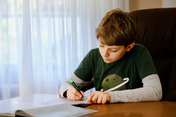 Un ragazzo della scuola felice che lavora sodo facendo i compiti durante la quarantena per una pandemia coronarica. Bambino sano che scrive con la penna, rimanendo a casa. Concetto di istruzione a casa — Foto Stock