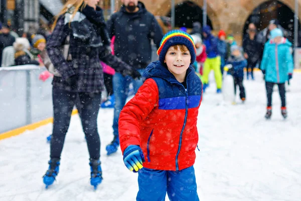 Glad liten pojke i färgglada varma kläder skridskor på en rinka av julmarknad eller rättvis. Friska barn som har roligt på skridskor. Många firar semester och har aktiv vinterfritid — Stockfoto