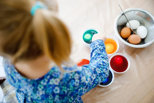 Primo piano della bambina che colora le uova per Pasqua. Primo piano del bambino che guarda sorpreso le uova colorate colorate, celebrando la vacanza con la famiglia. Dall'alto, volto non riconosciuto. — Foto Stock