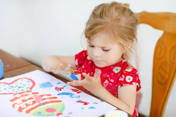 Little creative toddler girl painting with finger colors a fish. Active child having fun with drawing at home, in kindergaten or preschool. Education and distance learning for kids. Creaitve activity. — Stock Photo, Image
