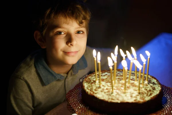 Чарівний щасливий світлий маленький хлопчик, який святкує свій день народження. Дитина дме свічки на домашньому запеченому торт, в приміщенні. День народження для школярів, сімейне святкування — стокове фото