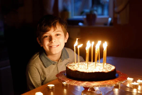 Entzückend glücklicher blonder kleiner Junge, der seinen Geburtstag feiert. Kind bläst Kerzen auf selbstgebackenem Kuchen, drinnen. Geburtstagsfeier für Schulkinder, Familienfeier — Stockfoto