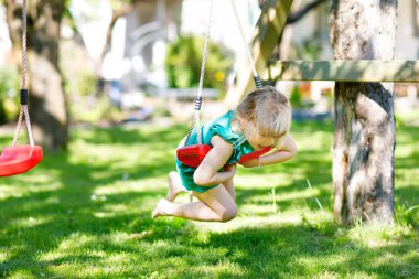 Küçük mutlu anaokulu kızı salıncakta salıncakta sallanıyor. Güneşli yaz gününde sallanan sağlıklı bir çocuk. Dışarıda çocuk aktivitesi, gülen çocuk.