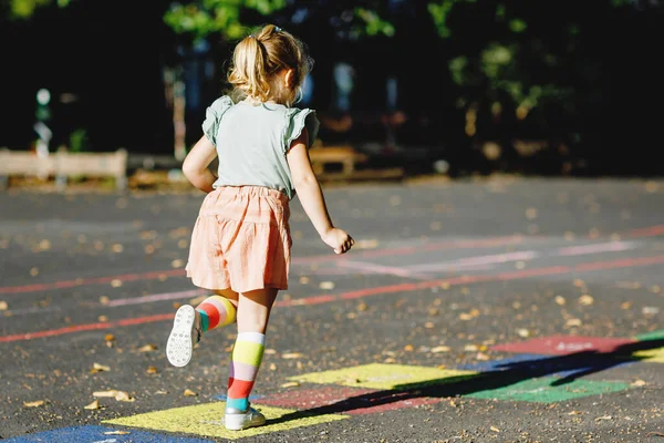 Cute little toddler girl playing hopscotch game drawn with colorful chalks on asphalt. Little active child jumping on playground outdoors on a sunny day. Summer activities for children. — Stock Photo, Image