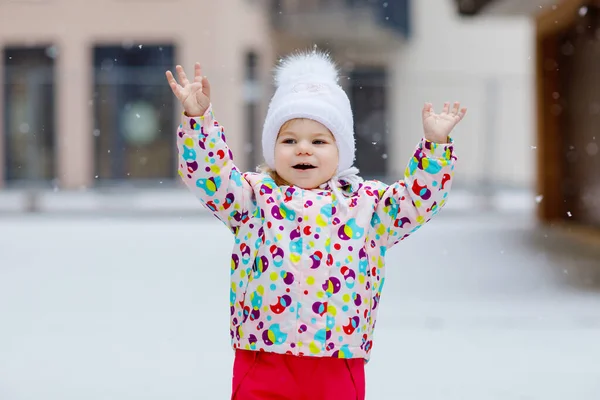 Porträtt av en liten flicka som går utomhus på vintern. Söta småbarn som äter sött godis. Barn har roligt på kall snö dag. Bär varm baby färgglada kläder och hatt med kulor. — Stockfoto