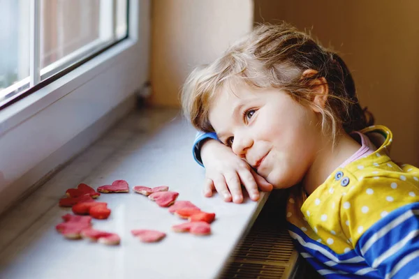 Schattig klein meisje door het raam met veel deeg harten als geschenk voor Valentijnsdag, Moederdag of verjaardag. Schattig vrolijk lachend kind binnen. — Stockfoto