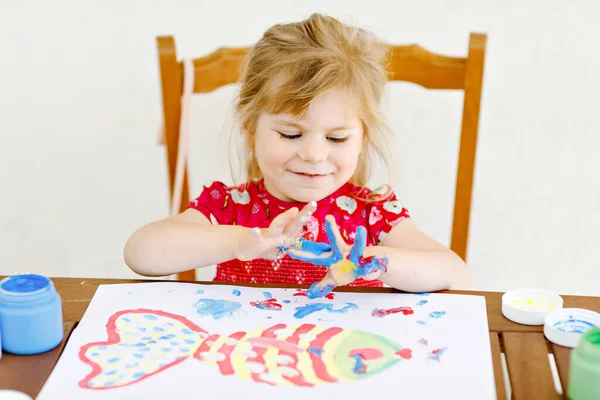 Little creative toddler girl painting with finger colors a fish. Active child having fun with drawing at home, in kindergaten or preschool. Education and distance learning for kids. Creaitve activity. — Stock Photo, Image