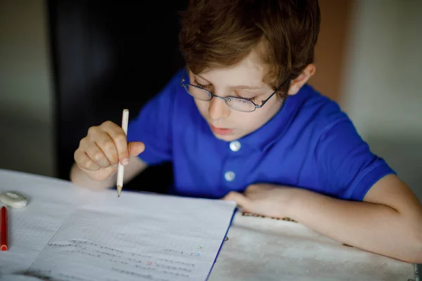 Retrato de menino com óculos em casa fazendo trabalhos de casa, escrevendo cartas com canetas coloridas. Criança a fazer exercício, dentro de casa. Escola primária e educação, conceito de escola em casa. — Fotografia de Stock
