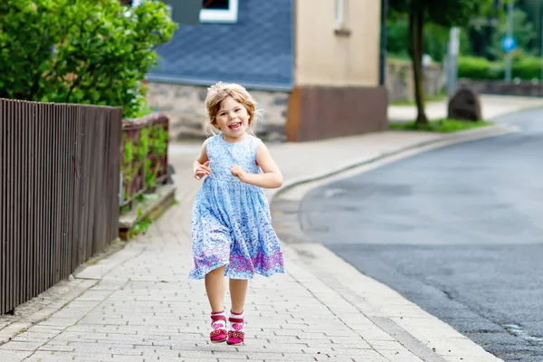 Glad liten flicka som springer på gatan i stan, utomhus. Roligt förskolebarn bygga ha kul med att springa, promenera, hoppa på solig sommardag. Aktiv familjesemester på sommaren. — Stockfoto