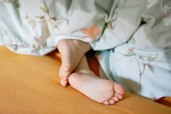 Childs legs are covered with white bed linen. The warmth of home comfort. Feet of little small girl.