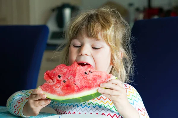 Mała przedszkolanka jedząca świeży czerwony arbuz. Maluch gryzie dojrzałe zdrowe owoce. Kid korzystających przekąski w kuchni domowej, w pomieszczeniach. — Zdjęcie stockowe