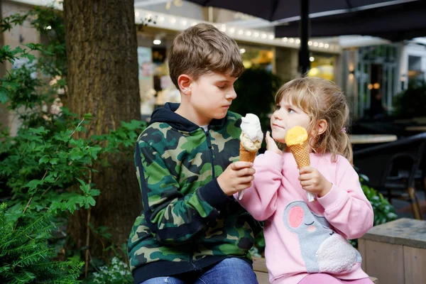 Маленькая дошкольница и школьник едят мороженое в вафельном рожке Счастливые дети, брат и сестра едят десерт из мороженого. Семья в городе. Братья и сёстры в любви. — стоковое фото