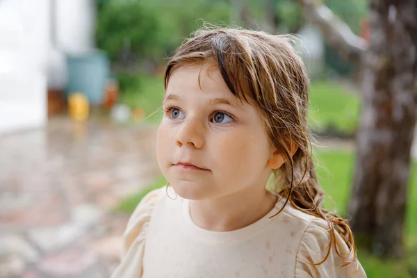 Little preschool girl running through heavy summer rain in garden. Happy smiling wet toddler child having fun with splashing and jumpin in puddles. Activity for children on rainy weather day. — Stock Photo, Image