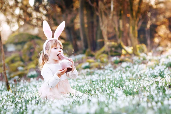 可爱的小女孩，带着复活节兔子的耳朵，在阳光灿烂的春天的森林里，在户外吃着令人窒息的人形食物。带着许多雪花的可爱的快乐的孩子。春天，基督教节日的概念. — 图库照片