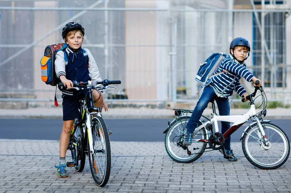 Dos niños de la escuela en casco de seguridad con bicicleta en la ciudad con mochilas. Niños felices en ropa colorida en bicicleta en bicicletas de camino a la escuela. Manera segura para los niños al aire libre a la escuela —  Fotos de Stock