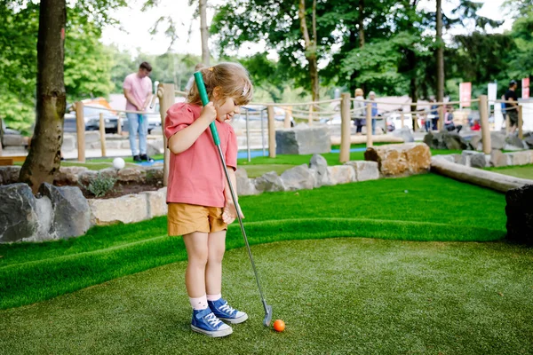 Menina pré-escolar bonito jogar mini golfe com a família. Criança feliz se divertindo com a atividade ao ar livre. Desporto de verão para crianças e adultos, ao ar livre. Férias em família ou resort. — Fotografia de Stock