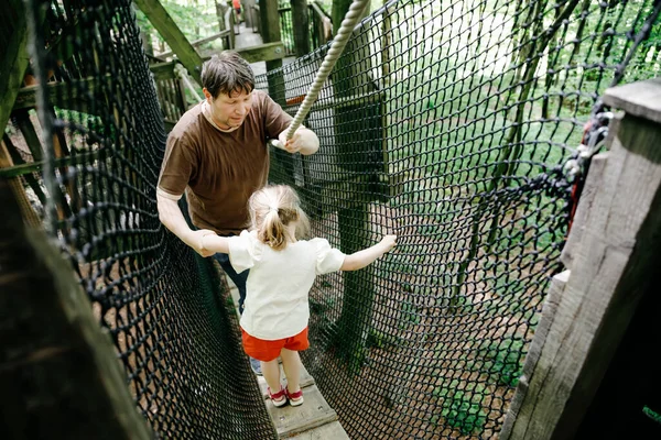 Liten förskoleflicka och far går på hög trädkronastig med trägång och rep. Glad aktiv barn och pappa, ung man utforskar trädtoppsbana. Rolig aktivitet för familjer utomhus — Stockfoto