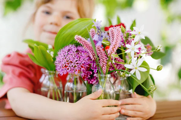 Close up de menina pré-escolar com buquê de flores em casa. Close-up de criança e flores coloridas de verão jardim em pequenas garrafas com água. Closeup de flores em cores do arco-íris. — Fotografia de Stock