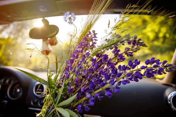 Closeup of driving in cabriolet car on sunny summer day. Couple traveling or having romantic date in cabrio. Woman holding lupines flowers bunch. Sunset, happiness, freedom. — Stock Photo, Image