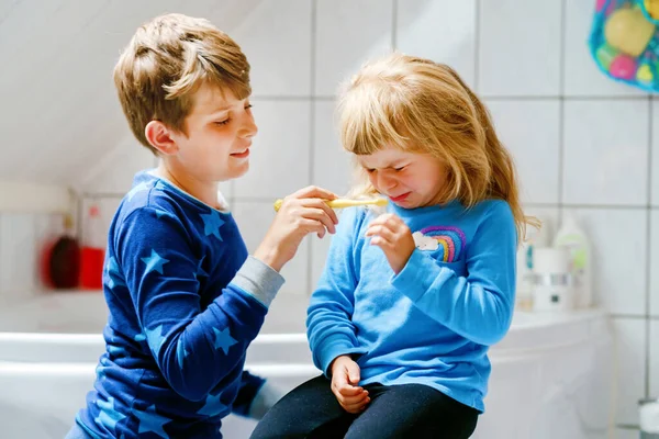 Klein kleuterschoolmeisje en een scholier die tanden poetst. Broer die zusters tanden leert poetsen. Verdrietig huilend kind. Twee kinderen en 's morgens tandartsroutine. Familie binnen. — Stockfoto