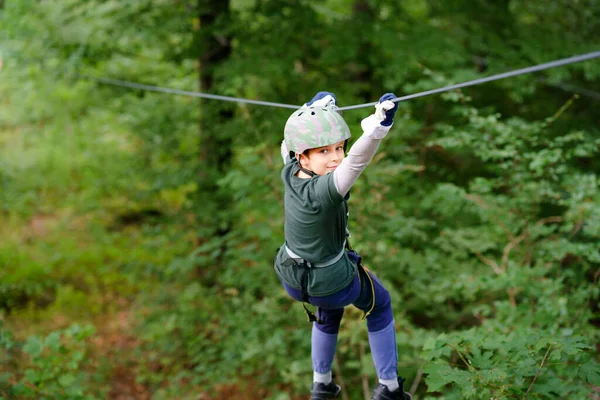 Шкільний хлопчик у лісовому парку. Дитина-акей, дитина в шоломі піднімається по високій мотузці. Навички спритності та скелелазіння на відкритому повітрі для дітей. Активність на відкритому повітрі для дітей та сімей . — стокове фото