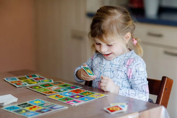 Opgewonden lachende schattige peuter meisje spelen foto kaartspel. Gelukkige gezonde kind training geheugen, denken. Creatief binnen vrije tijd en onderwijs van het kind. Gezinsactiviteiten thuis. — Stockfoto