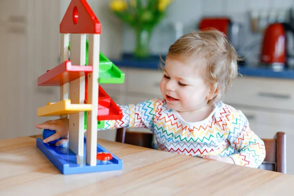 Kleine Mädchen spielen zu Hause oder im Kinderzimmer mit Lernspielzeug. Fröhliches gesundes Kleinkind, das Spaß an der bunten Kugelbahn aus Holz hat. Kind lernt Bälle zu halten und zu rollen. Motorische Bildung. — Stockfoto